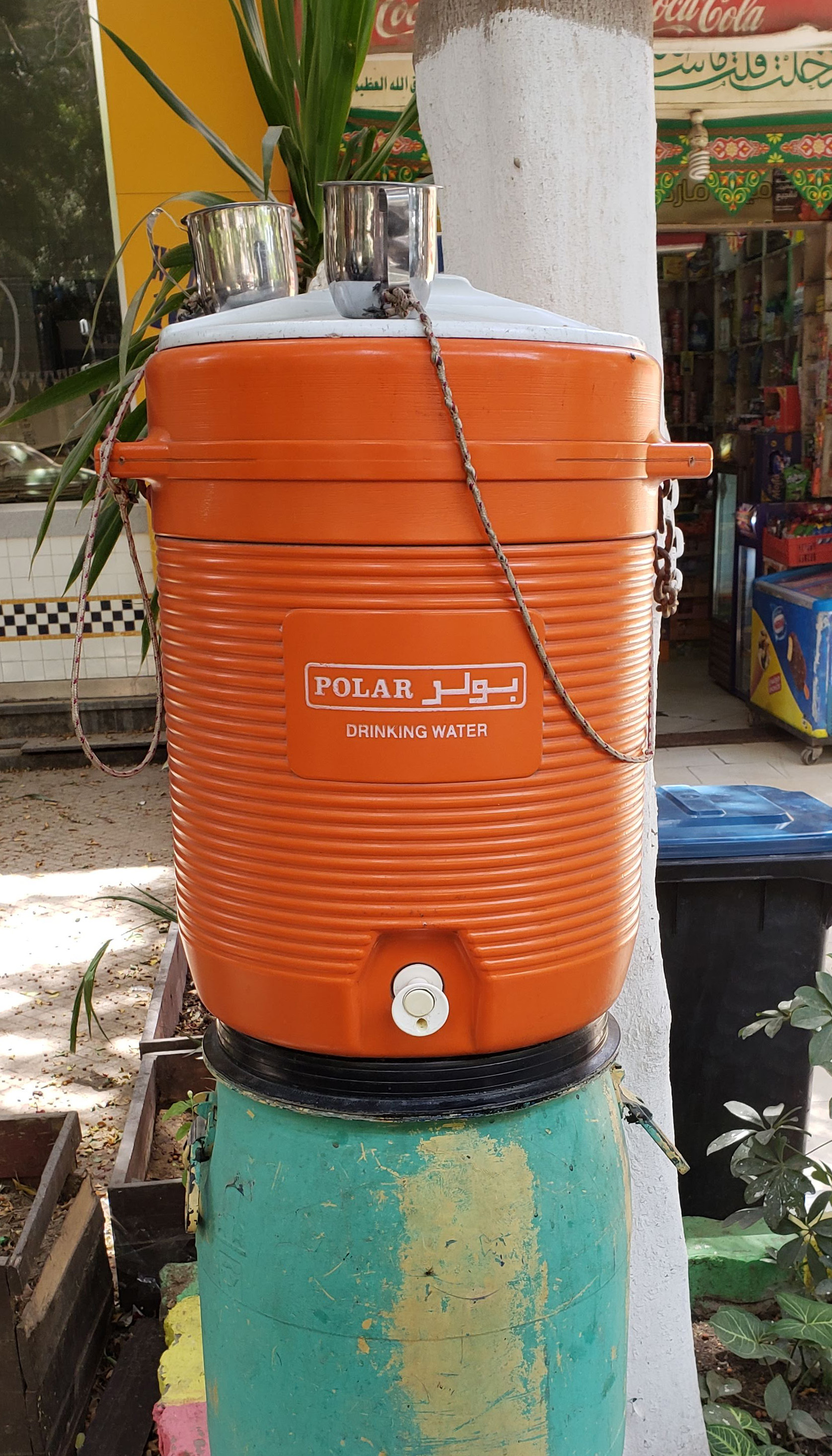 A red plastic water cooler outside of a shop.